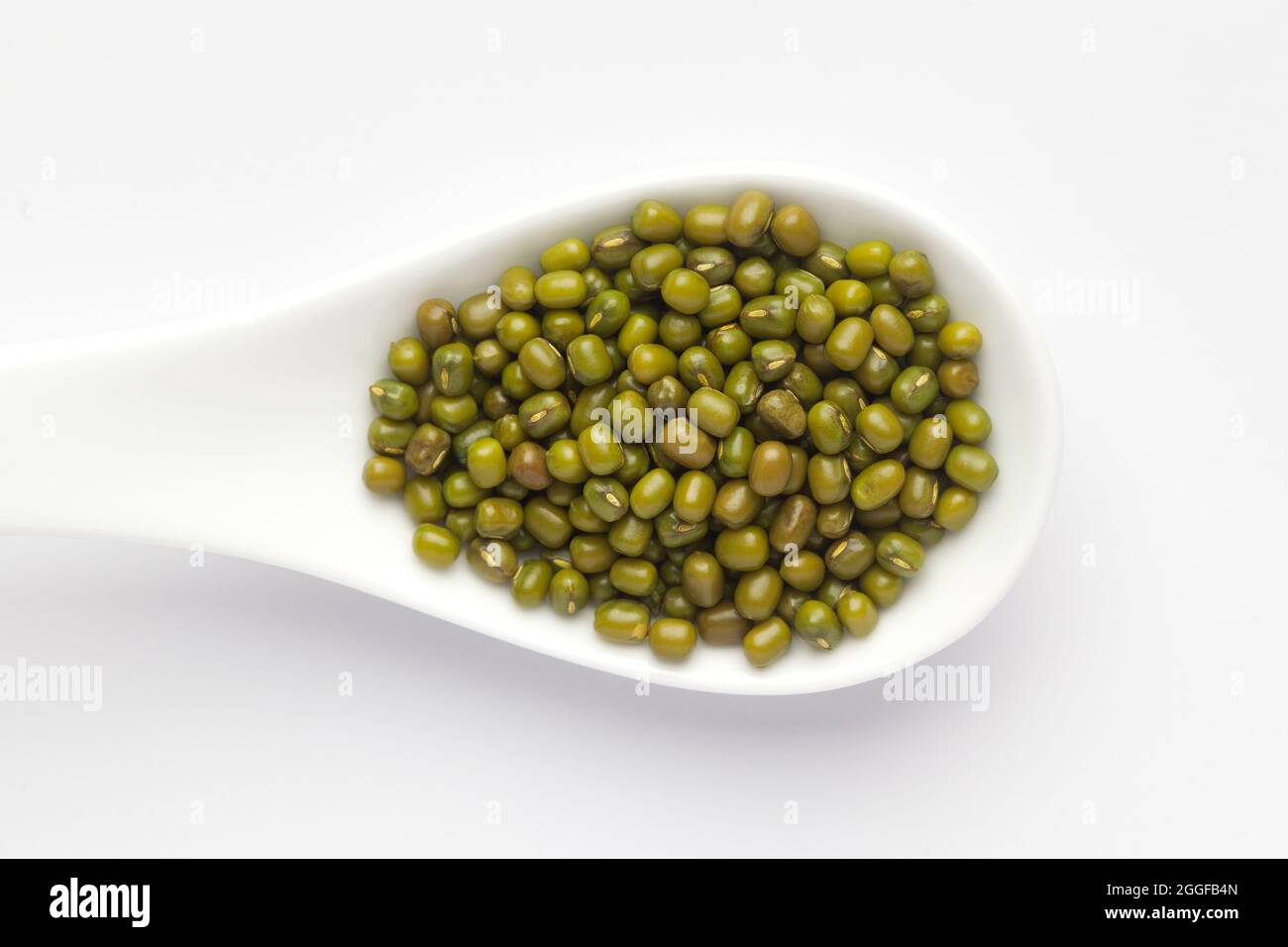 Macro primo piano di gram verde biologico (Vigna radiata) o di moong verde intero dal su un cucchiaio per zuppa di ceramica bianca. Vista dall'alto Foto Stock