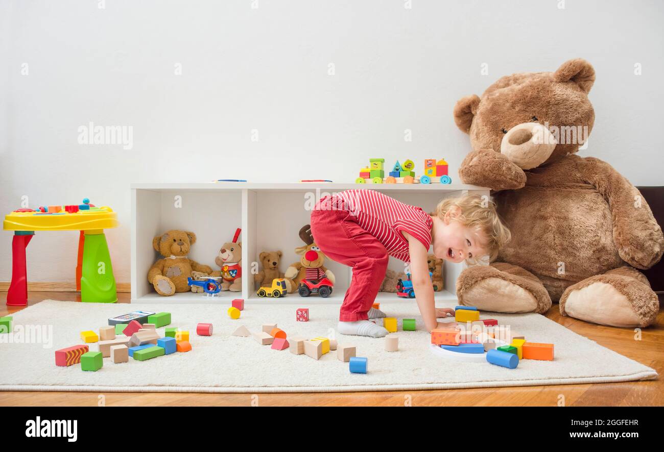 Dolce ragazzo felice bambino divertirsi a casa giocando con il suo orsacchiotto gigante e colorati blocchi di legno e giocattoli, sul pavimento. Foto Stock