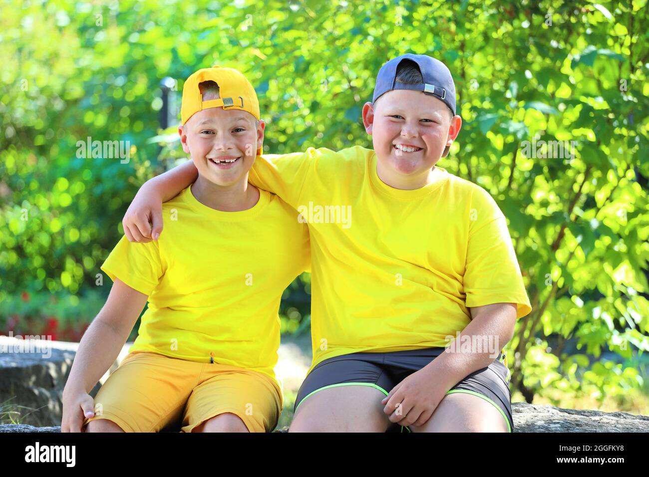 Due ragazzi in T-shirt gialle che abbraccia seduti nel parco. Foto di alta qualità Foto Stock