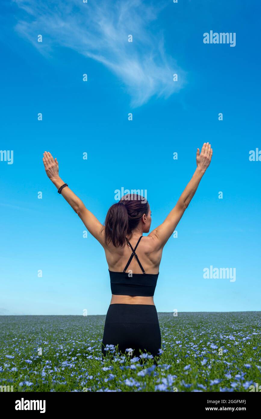 Donna sportiva con le braccia sollevate che si allungano in un campo con cielo blu. Foto Stock