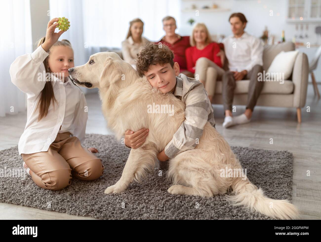 Adorabili bambini che giocano e abbracciano il cane mentre la loro grande famiglia si rilassa sul divano nel soggiorno. I bambini si divertono con Golden Retriever sul piano A. Foto Stock