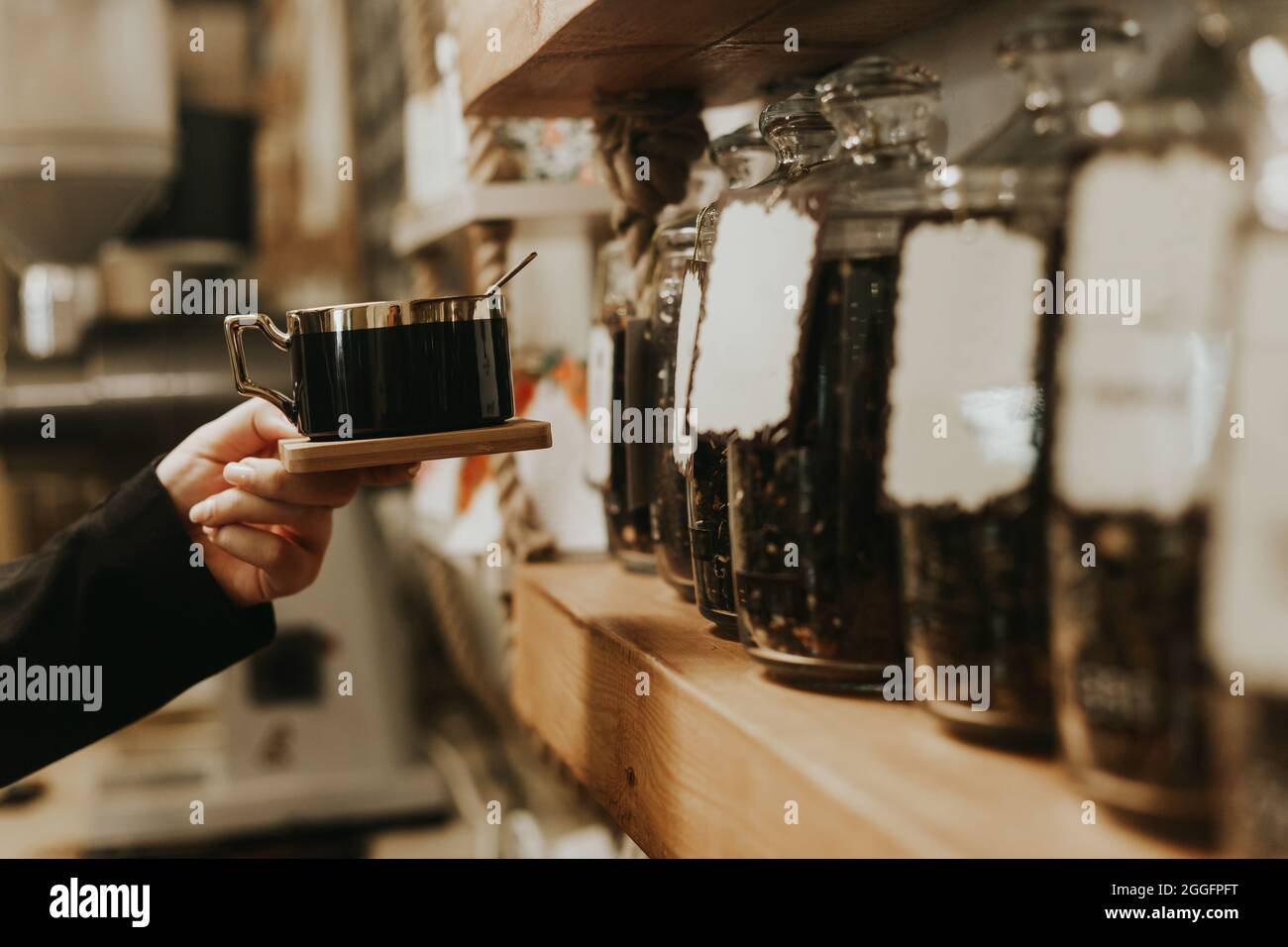 Lifestyle shot di tazza da caffè femminile in coffee shop davanti agli scaffali Foto Stock