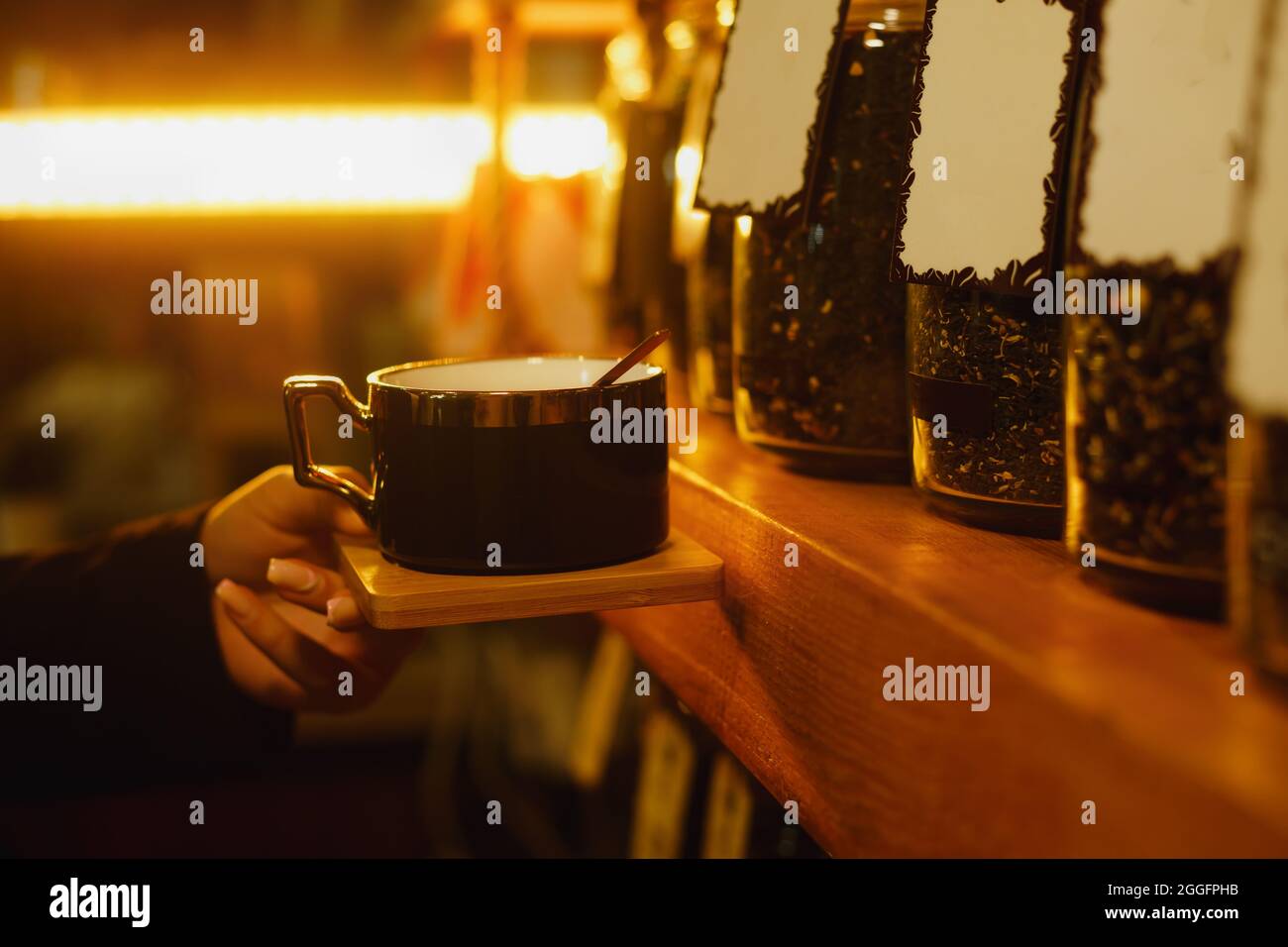 Primo piano di una tazza da caffè femmina che tiene la tazza di caffè davanti ai ripiani pieni di contenitori per la conservazione del caffè Foto Stock