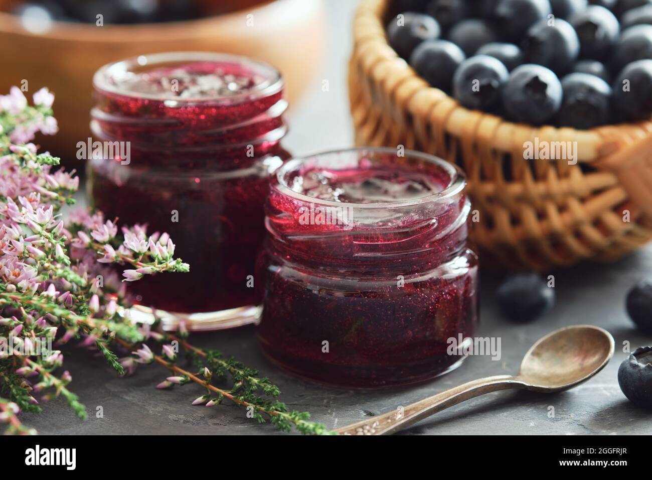 Due vasetti di marmellata di mirtilli, cestino con mirtilli freschi sul tavolo da cucina. Foto Stock