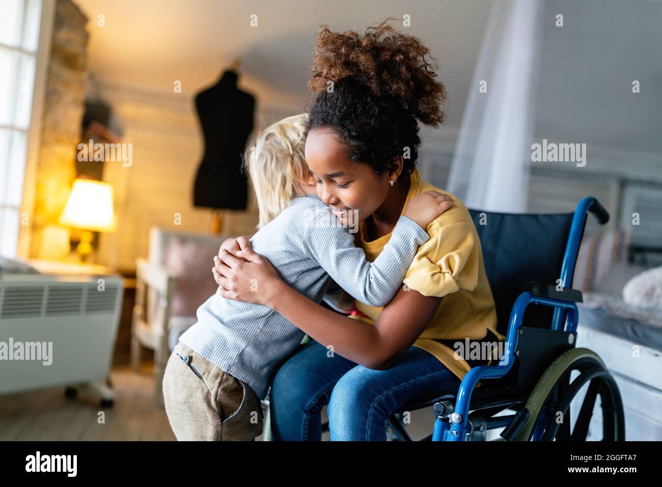 Bambina nera con disabilità in sedia a rotelle abbracciata con il fratello minore. Foto Stock