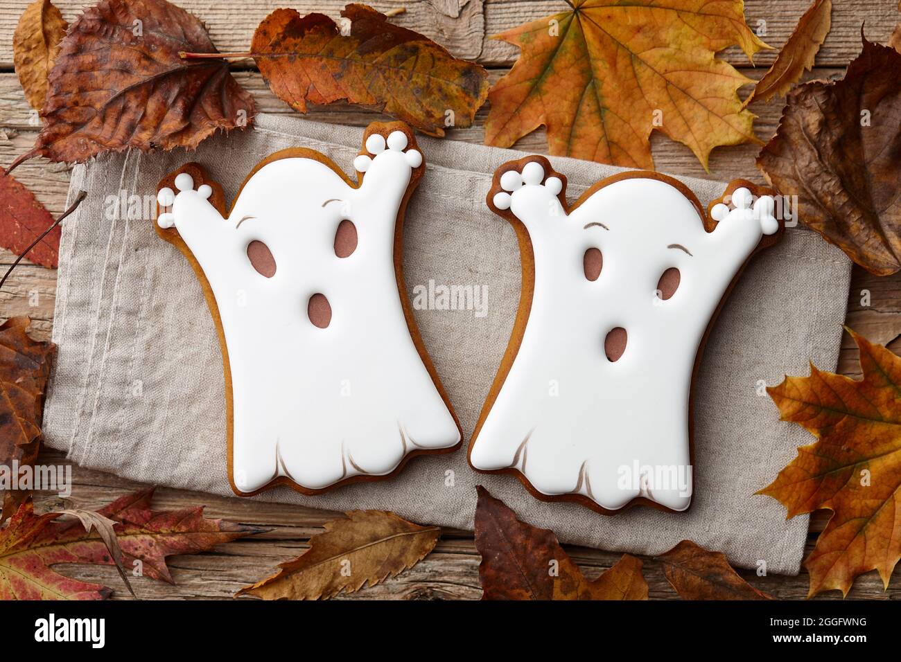 Biscotti di pan di zenzero di Halloween e foglie d'autunno su tavole di legno, fantasmi bianchi Foto Stock