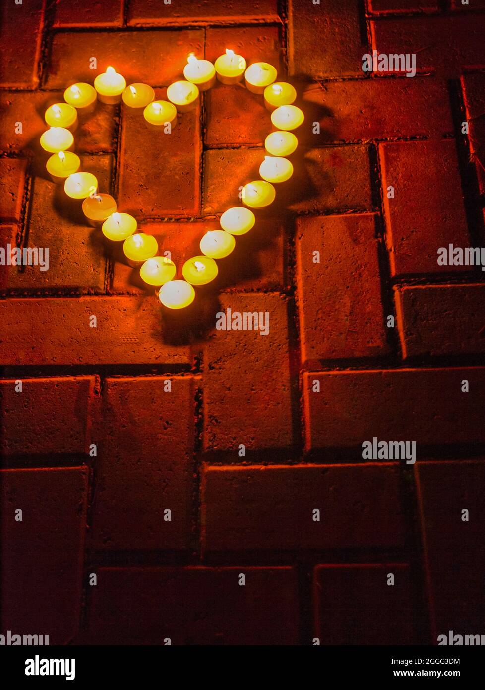 Colpo verticale di candele brucianti a forma di cuore su uno sfondo di mattoni. Foto Stock