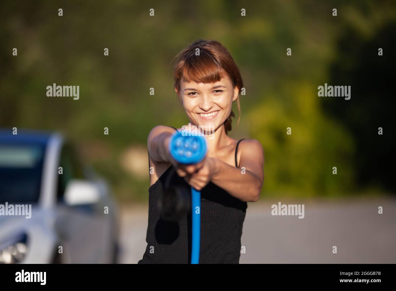 Bella ragazza giovane accanto a un'auto elettrica. Posa e fissaggio di un cavo di ricarica. Foto Stock