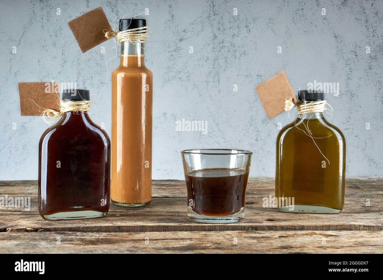 Bottiglie e vetro con liquore fatto a mano su tavola di legno con etichette vuote . Bevande alcoliche artigianali. Orizzontale Foto Stock