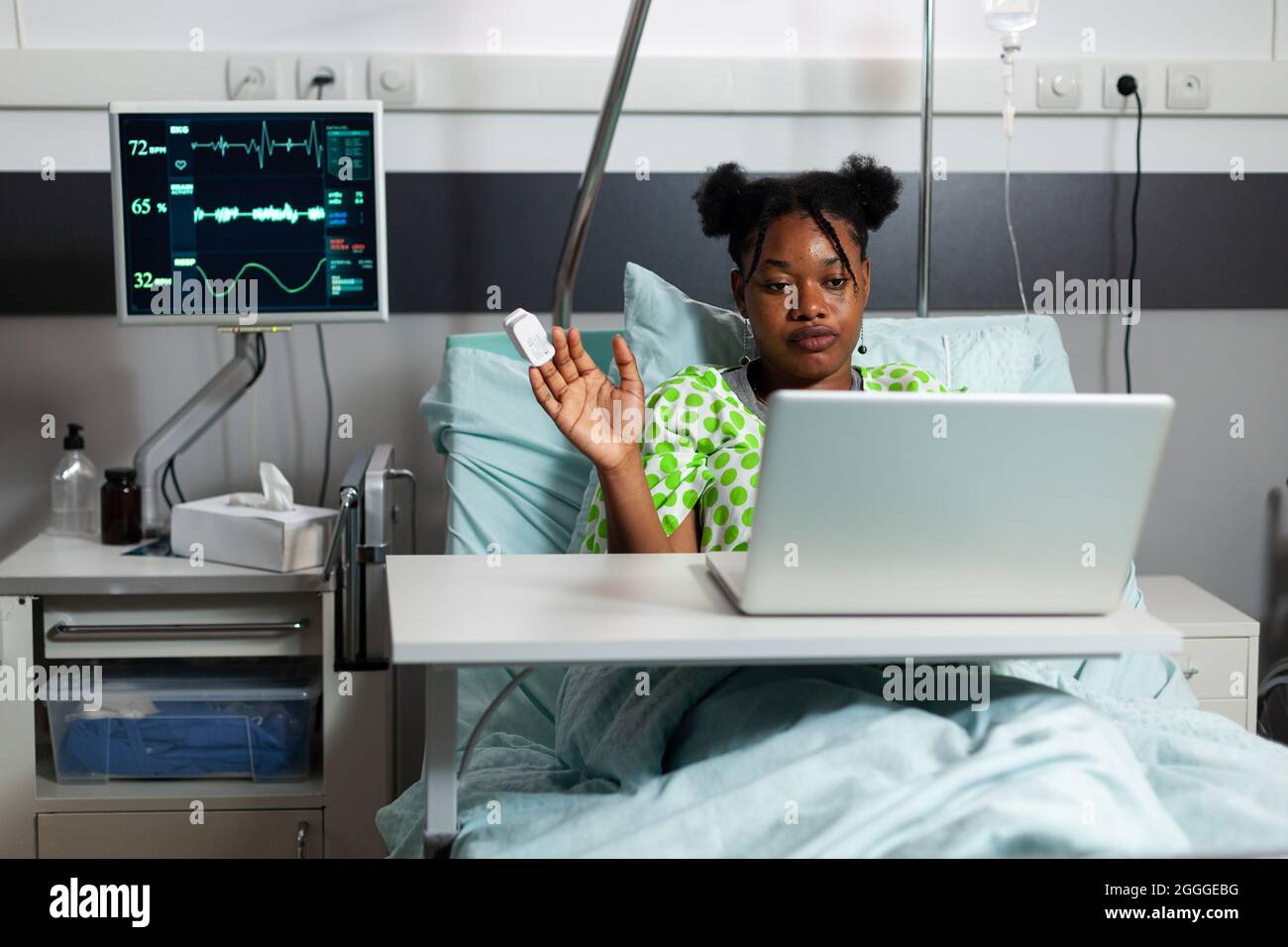 Ragazza afroamericana in ospedale reparto utilizzando la tecnologia di videochiamata su laptop. Giovane malato seduto a letto con moderno dispositivo di comunicazione e conferenza su connessione internet Foto Stock