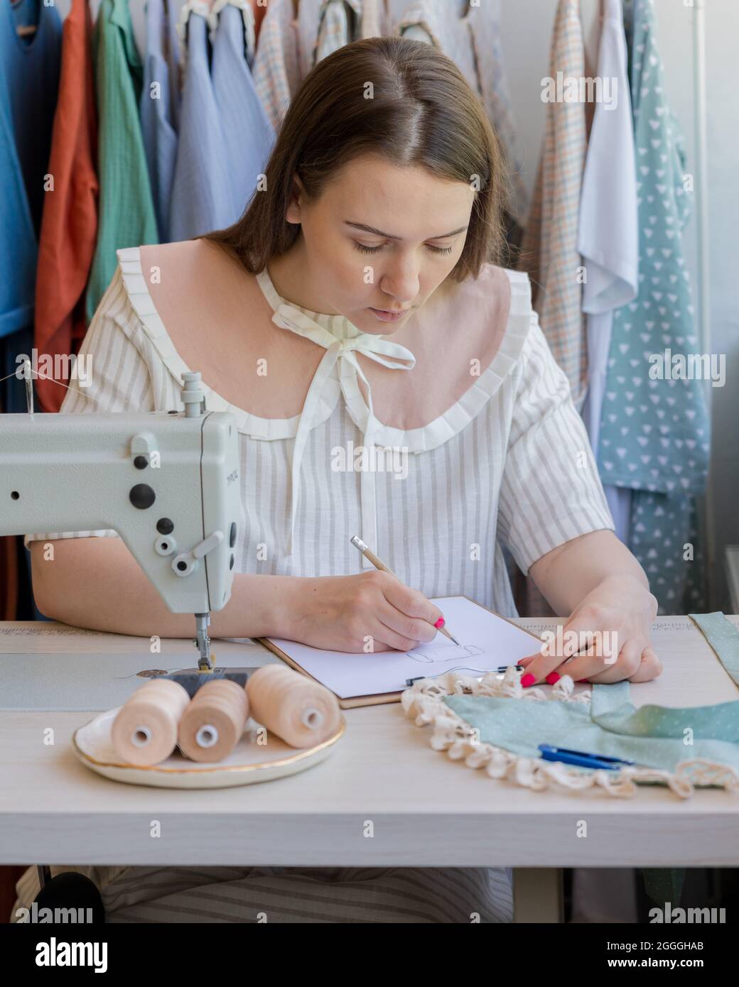 Stilista di moda disegno vestiti schizzo whie seduta al suo posto di lavoro con macchina da cucire Foto Stock
