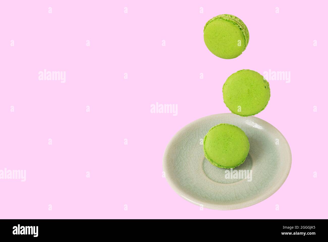 Pezzi di macaroni di pistacchio verde o di macaroni francesi che cadono su un piatto di ceramica verde. Concetti di fotografia di levitazione alimentare. Isolamento su rosa tenue b Foto Stock