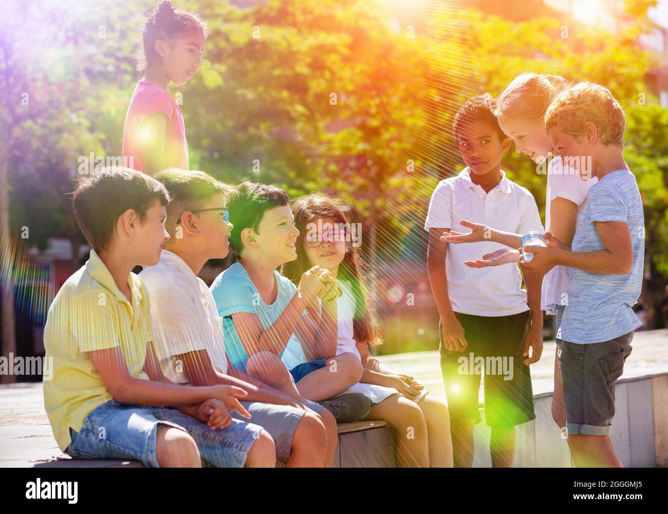 Gruppo di bambini allegri seduti su panca e che condividono segreti Foto Stock