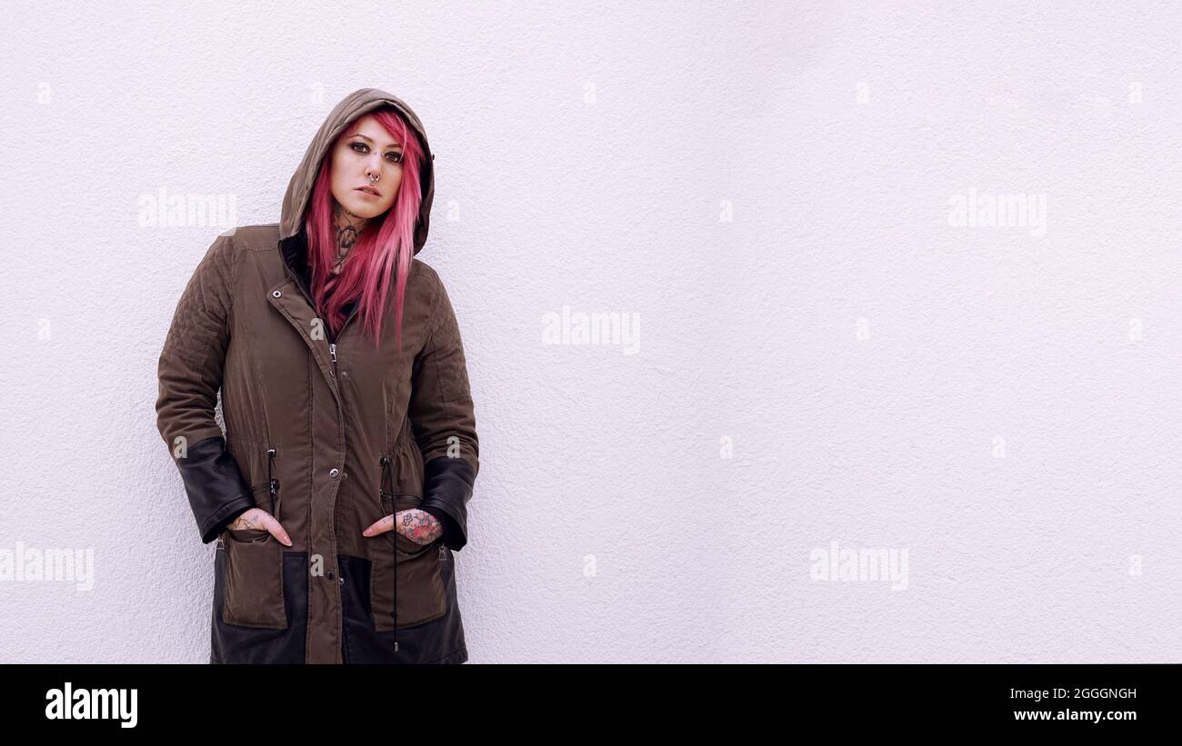 giovane donna con pelo rosa parka con cappuccio e tatuaggi contro la parete con spazio copia Foto Stock
