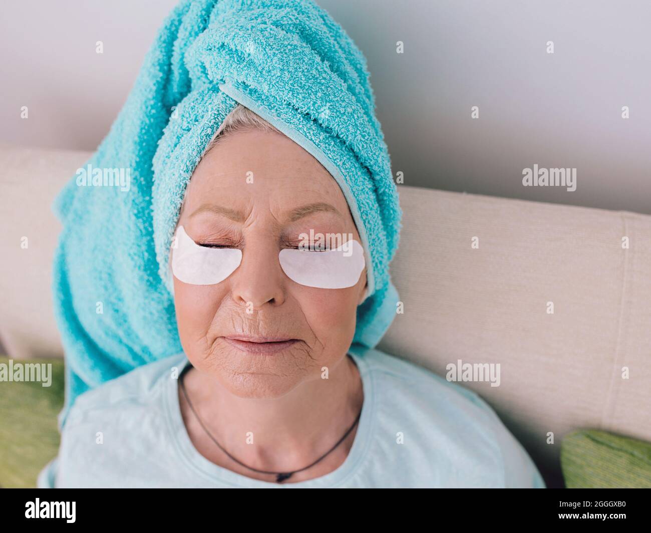 donna di stile caucasica anziana che si stende su una vettura con asciugamano blu su di lei ha avuto e collagene patch occhio. Anti età, stile di vita sano Foto Stock