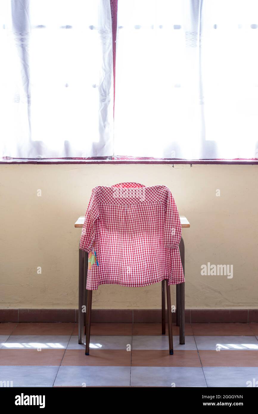 Fotografia del grembiule di un bambino su una sedia in un'aula scolastica.la foto è scattata in formato verticale. Foto Stock