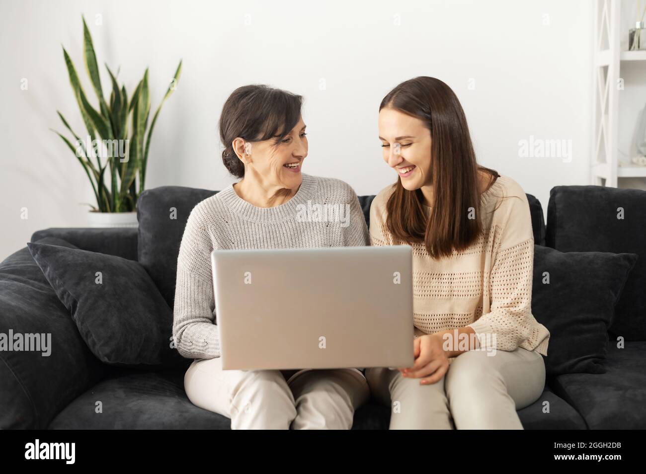 Due donne diverse generazioni trascorrere il tempo libero a casa, una madre anziana e una figlia adulta sta utilizzando un computer portatile. Una giovane donna spiega a donna matura come usare il computer, aiuta a inviare e-mail Foto Stock