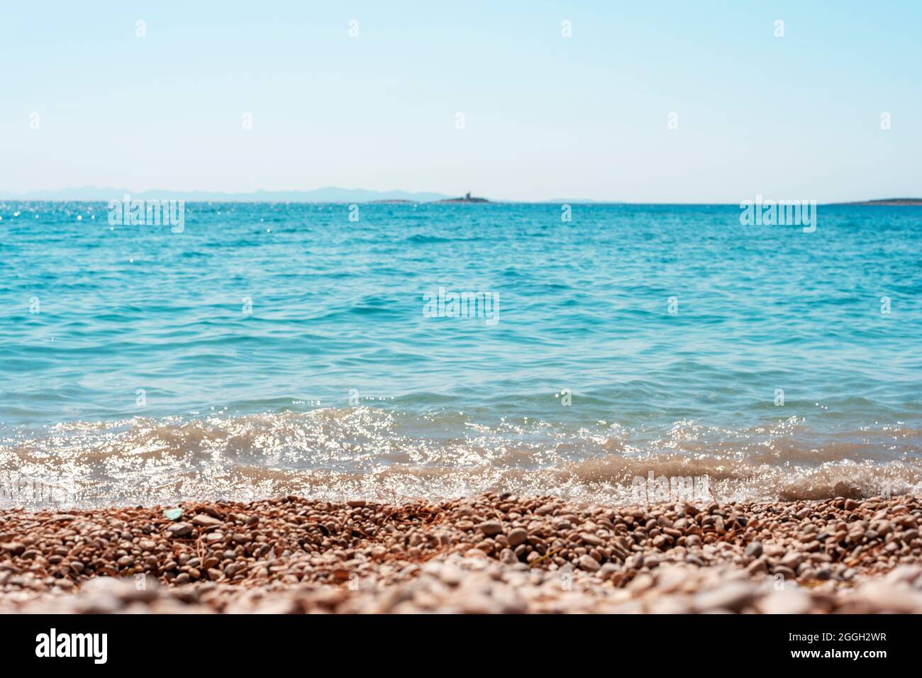 Bellissima spiaggia di ciottoli e mare blu con isole. Profondità di campo poco profonda. Foto Stock