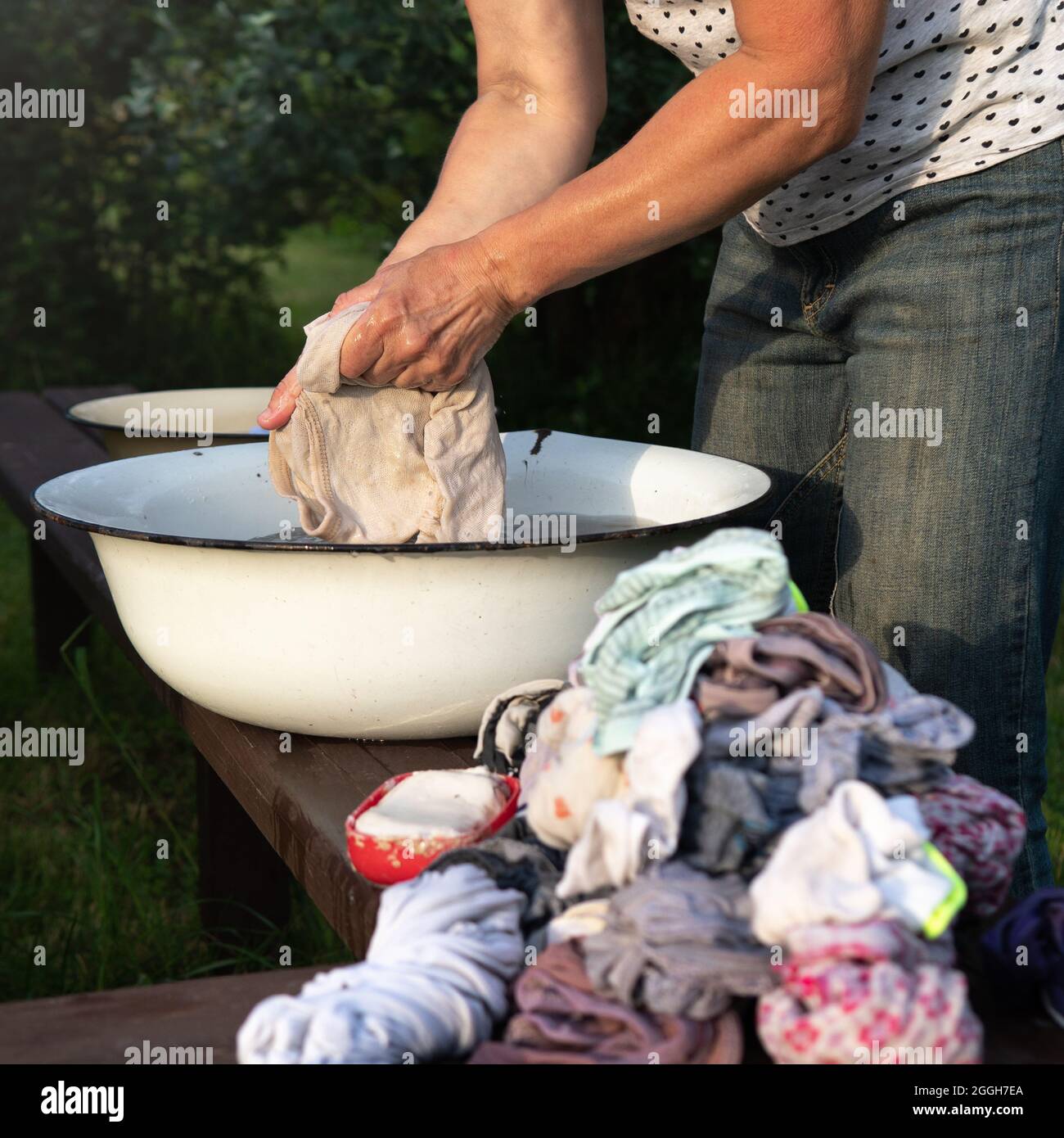La donna lava i vestiti con le mani nel vecchio bacino, risciacqua e poi  strizza la lavanderia lavata all'aperto in campagna in estate sera. Vista  laterale Foto stock - Alamy