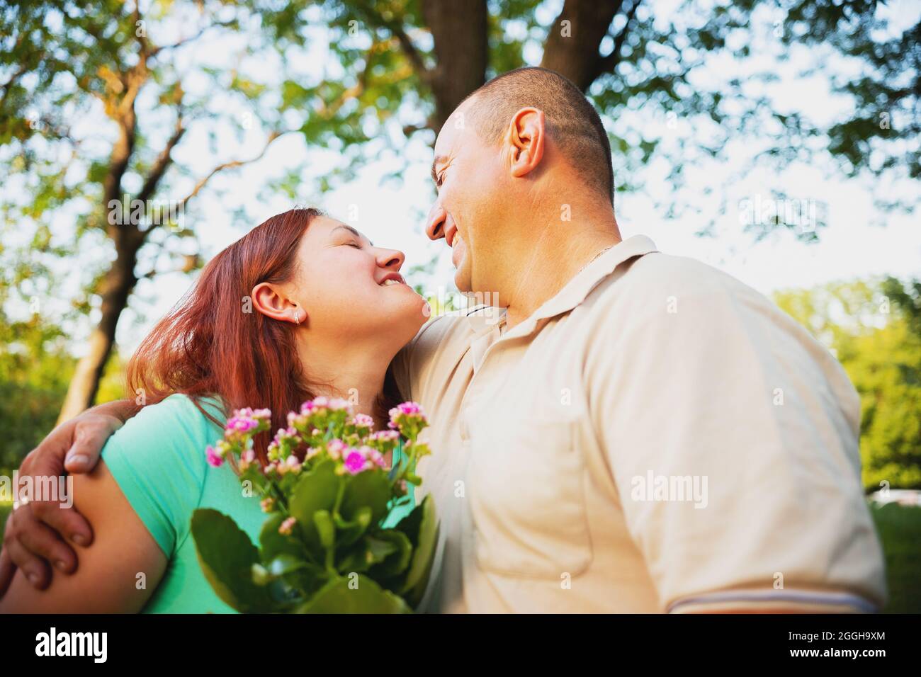 Felice coppia in amore avendo romantica data all'aperto guardandosi l'un l'altro e sorridendo, l'uomo ha dato la sua donna che ama i fiori e abbracciandola. Foto Stock