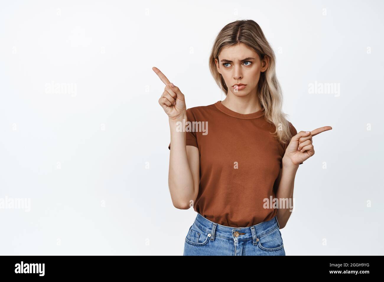 Ritratto di giovane donna sconvolta pointing, puntando lateralmente e guardando a sinistra a un'opzione, con deluso pointing volto espressione, sfondo bianco Foto Stock