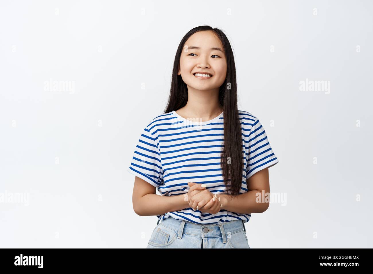 Immagine di una bruna sorridente ragazza asiatica che tiene le mani insieme, in piedi fiduciosa e professionale, guardando a sinistra il nome del marchio, in piedi su bianco Foto Stock