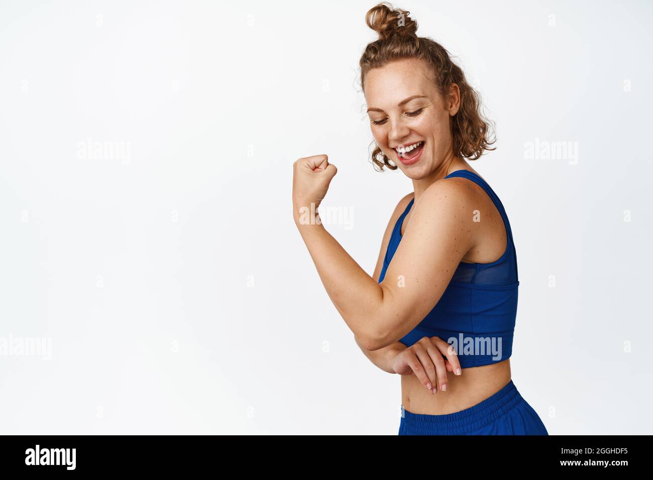 Lo sportivo sorridente mostra muscoli forti, bicipiti flettenti sul braccio, risultati di allenamento e palestra, in piedi su sfondo bianco Foto Stock