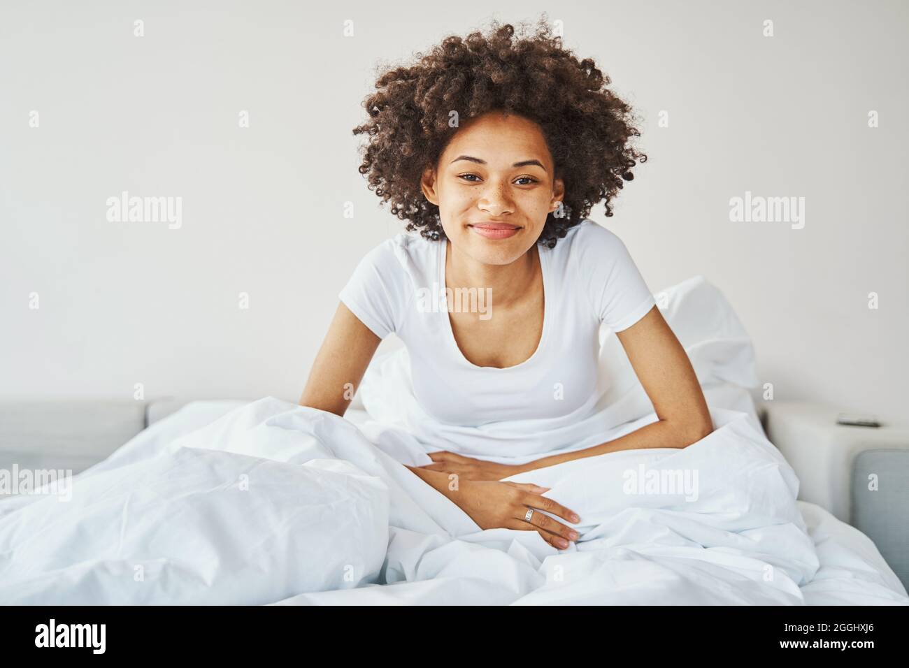 Felice attraente afroamericana donna seduta a letto Foto Stock