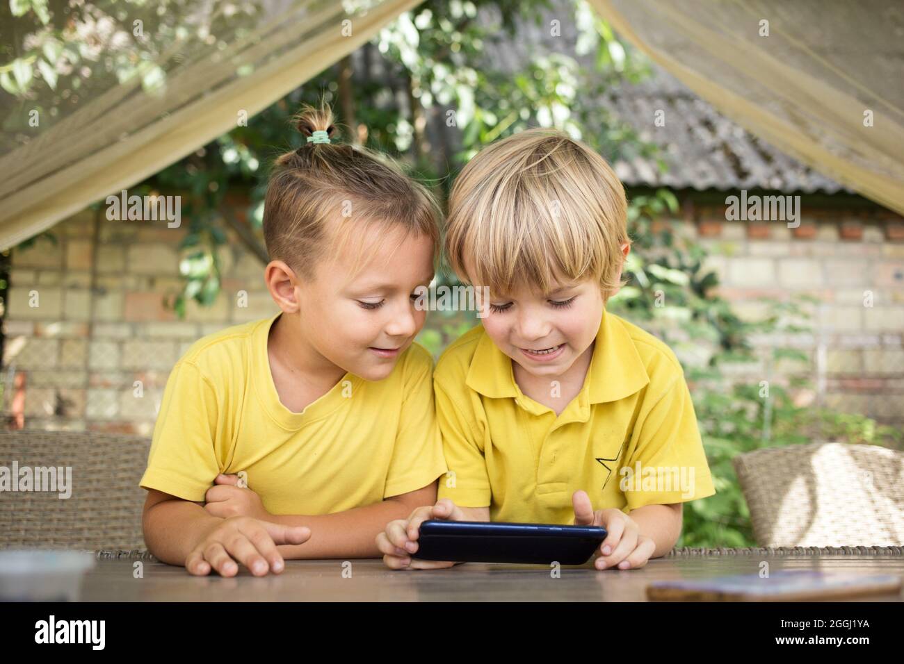 Ragazzi carini di 5 anni fratelli in magliette gialle guardano con interesse lo schermo del telefono di fronte a loro. Bambini moderni eta digitale curiosita Foto stock Alamy