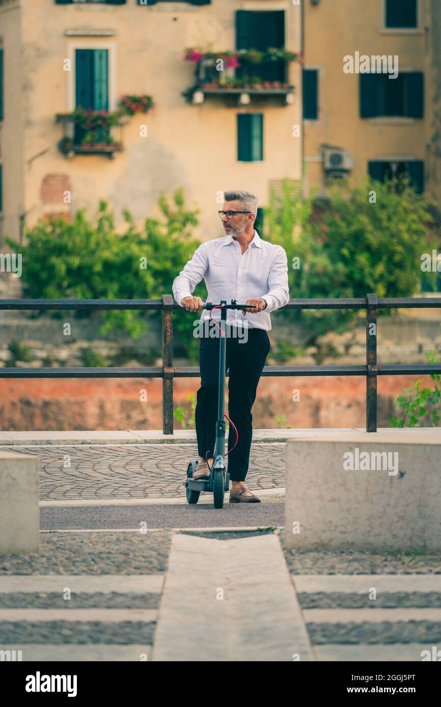 Bel uomo d'affari in tuta a guidare uno scooter elettrico mentre si viaggia per lavoro in città. Concetto di trasporto ecologico Foto Stock