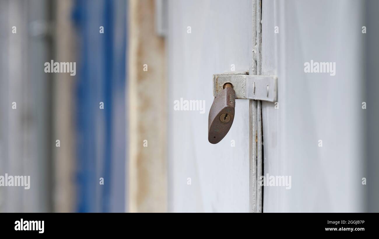 Lucchetto su sportello in metallo bianco, primo piano con profondità di campo ridotta e sfondo industriale sfocato. Foto Stock