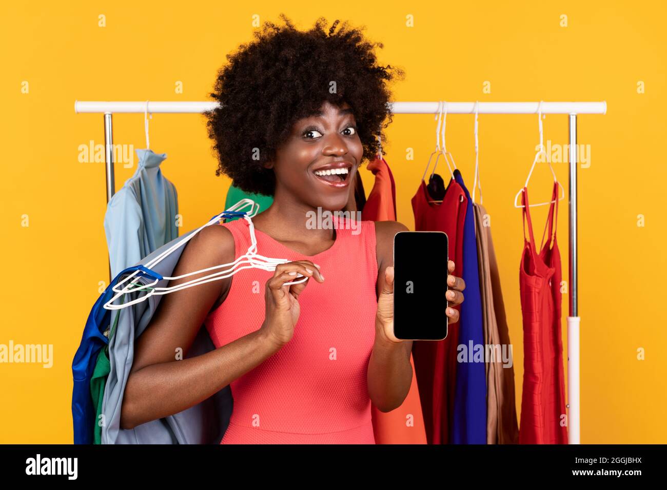 Eccitata Donna Shopaholic afroamericana che mostra schermo del telefono, sfondo giallo Foto Stock