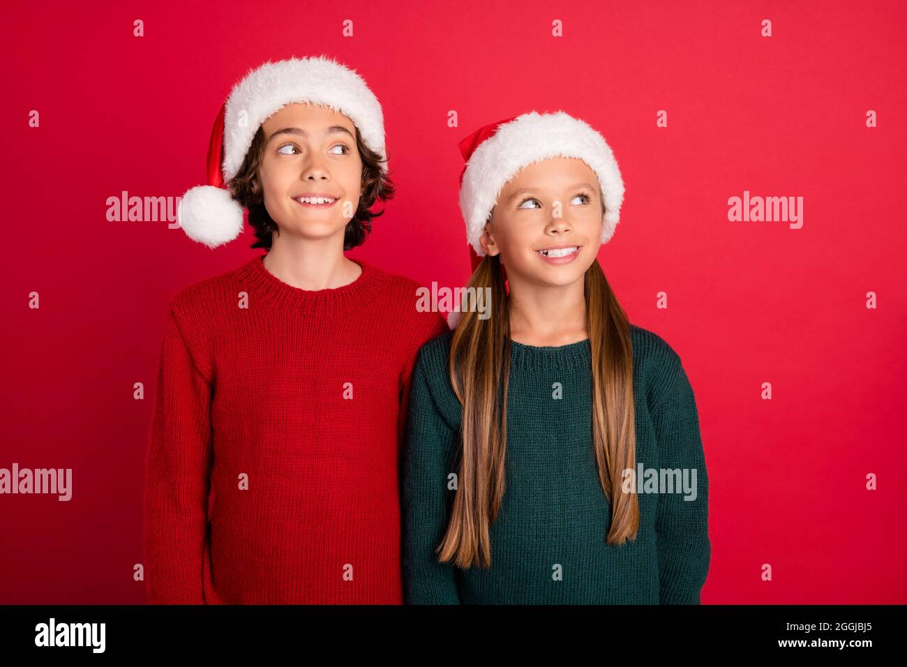 Ritratto di due amici allegri e attraenti che indossano un cappellino festale che fantasiizza isolato su sfondo rosso brillante Foto Stock