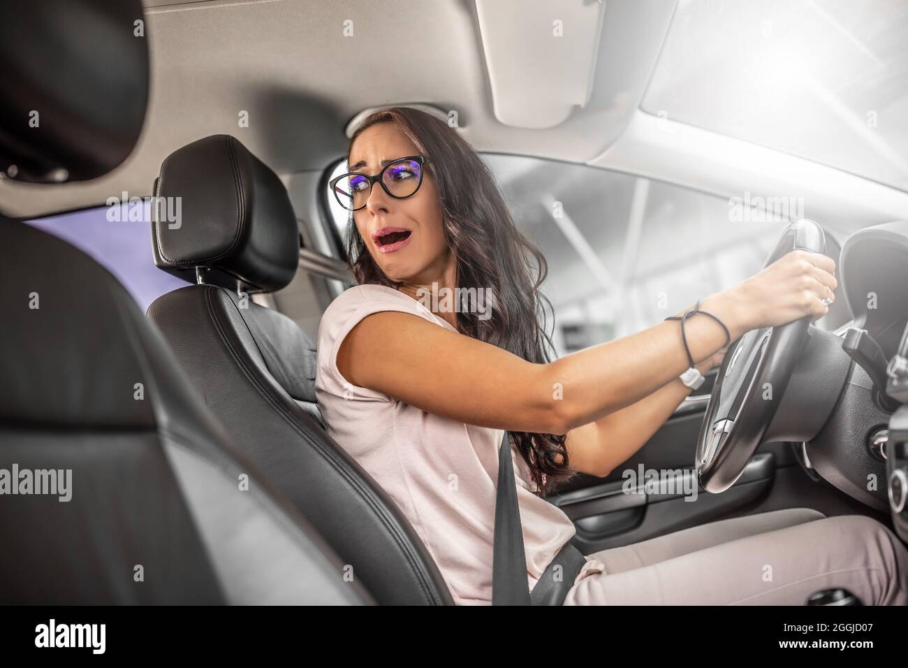 Il conducente inesperto con espressione facciale spaventata inverte l'auto guardando sopra la spalla. Foto Stock