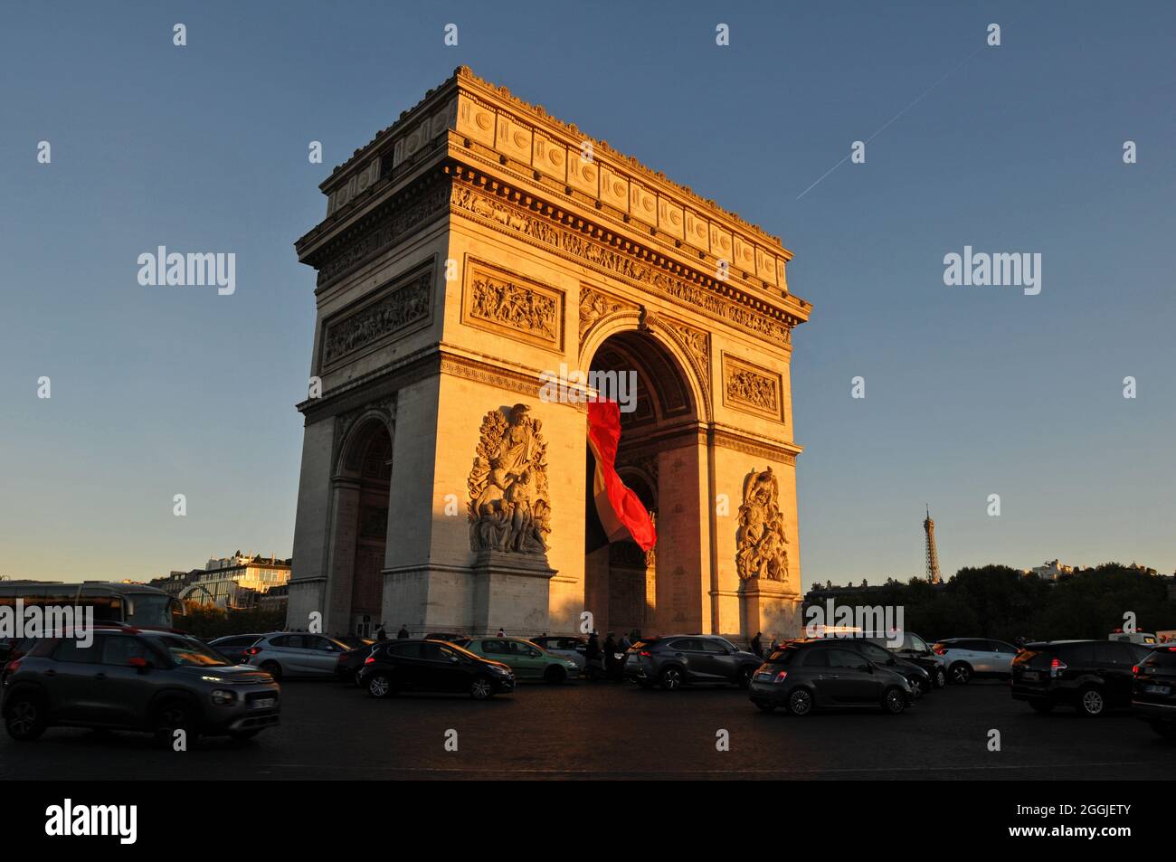 Il sole nel tardo pomeriggio illumina il punto di riferimento dell'Arco di Trionfo mentre il traffico scorre intorno al monumento in Place Charles de Gaulle di Parigi. Foto Stock