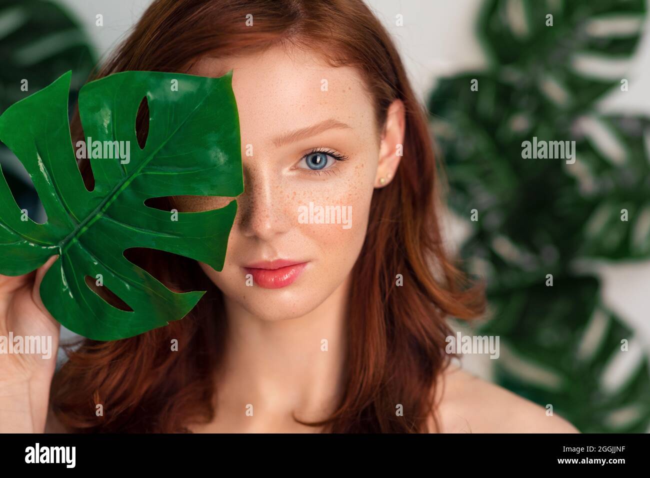 Headshot of Female posing Covering Eye with Monstera Leaf, studio Foto Stock