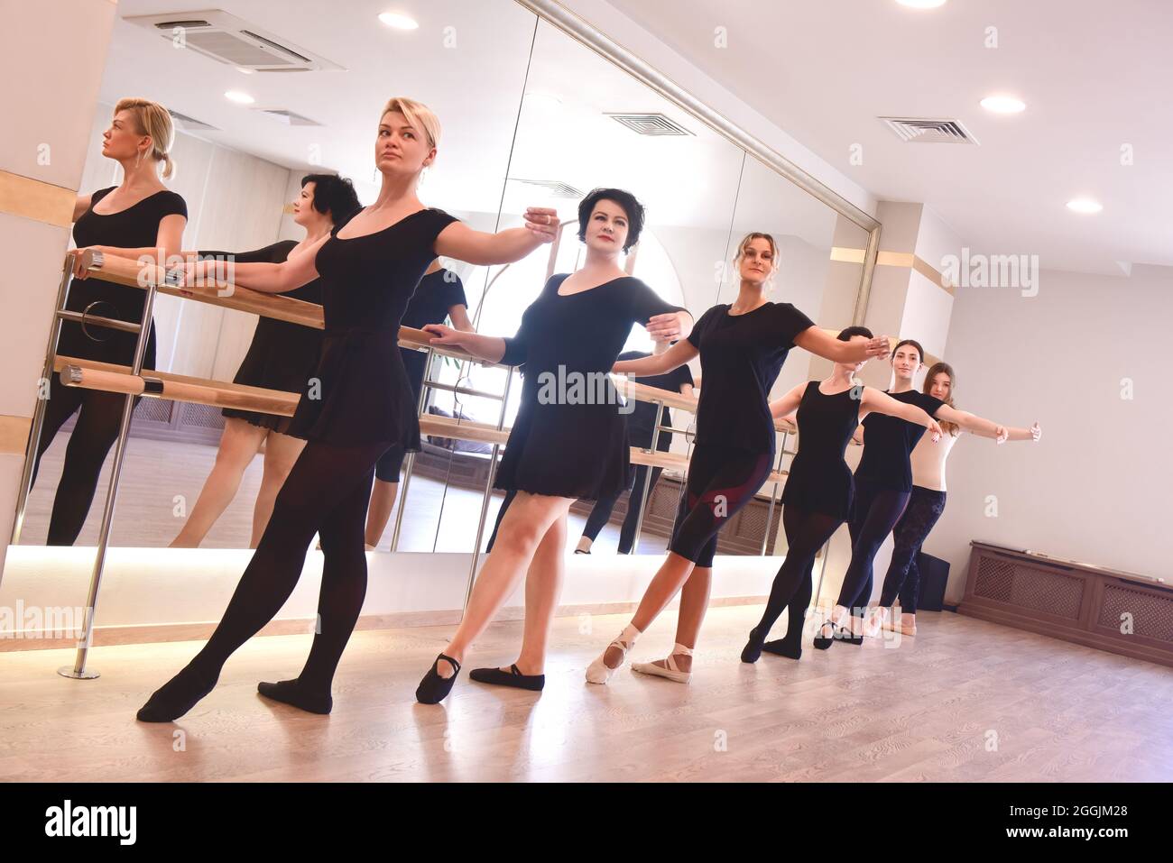 Un gruppo di donne ballerine esegue esercizi di balletto sollevando le braccia utilizzando il bar in palestra Foto Stock