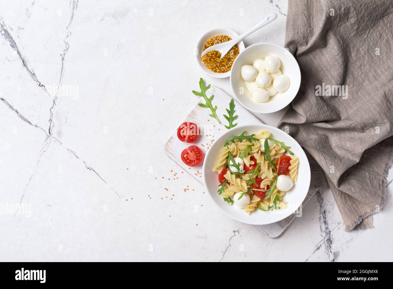 Vista dall'alto della gustosa pasta vegetariana con pomodori ciliegini, mozzarella di formaggio morbido, salsa di senape e foglie di rucola verde su sfondo bianco di marmo Foto Stock