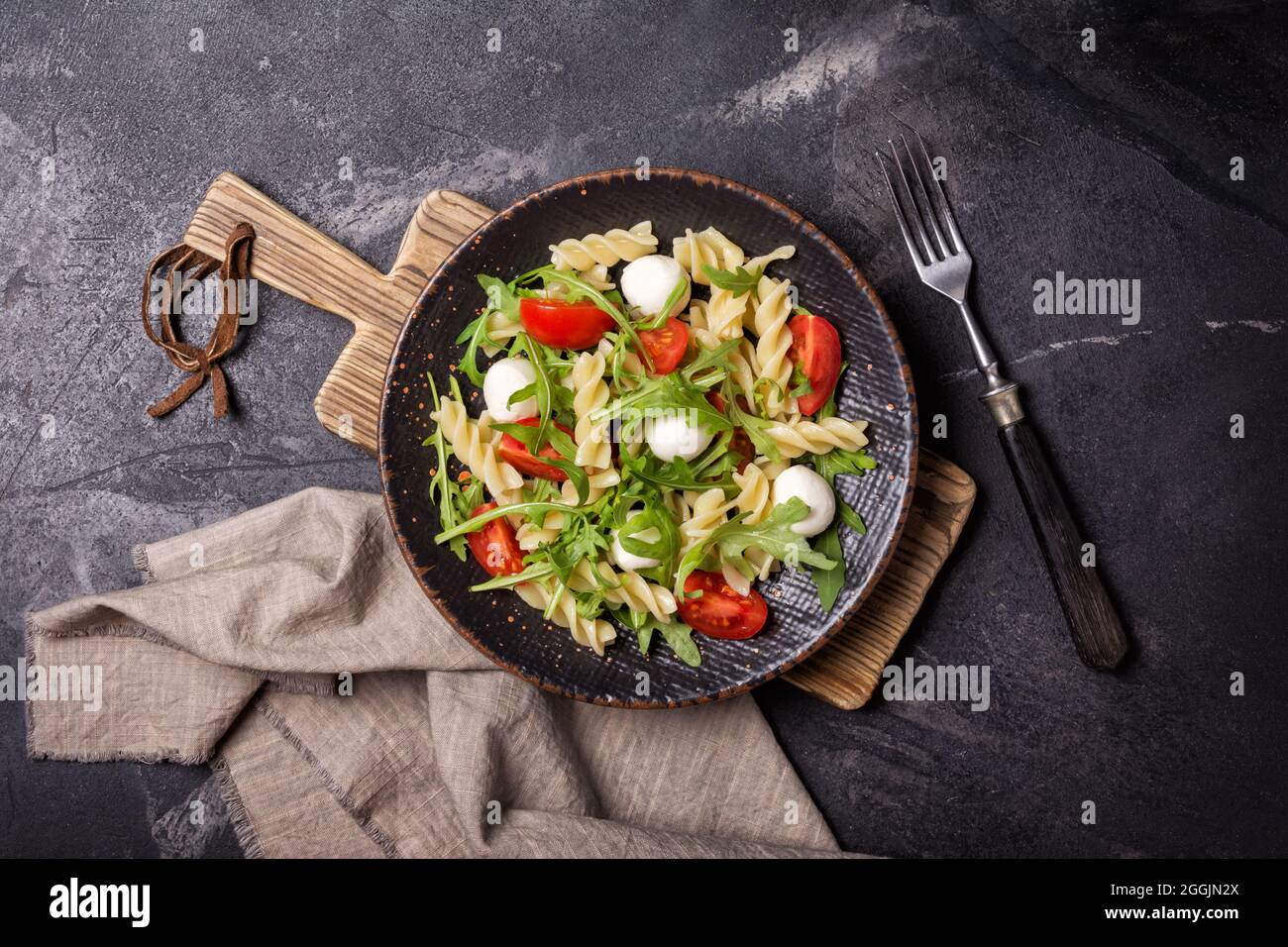 Vista dall'alto di gustosa pasta vegetariana con pomodori ciliegini, morbida mozzarella di formaggio e foglie di rucola verde su sfondo di marmo nero Foto Stock