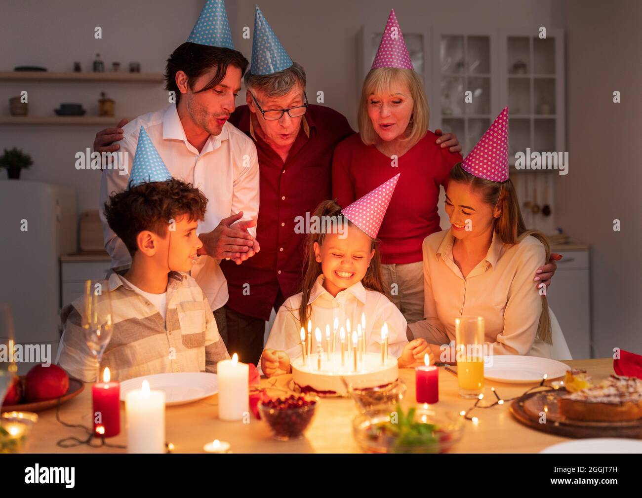 Gioiosa bambina che riceve gustosa torta di compleanno con candele di famiglia amorevole, festeggiando b-giorno a casa in serata Foto Stock