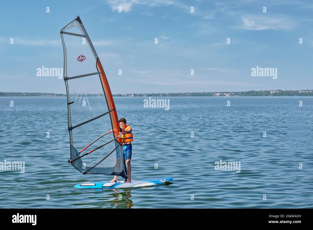 Corsi di windsurf. Ragazzo che galleggia a bordo con vela sul lago Foto Stock