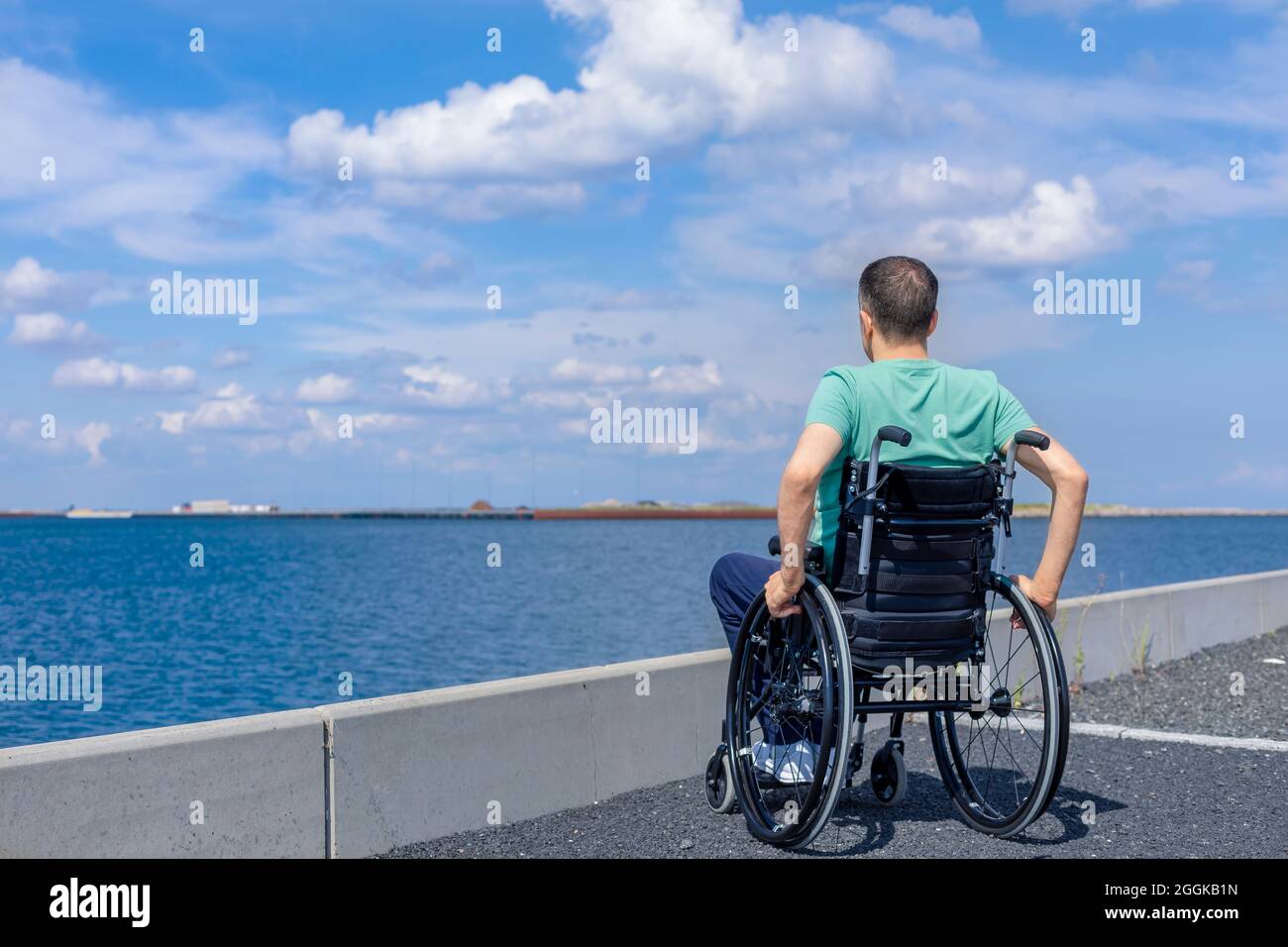 Uomo disabile in sedia a rotelle ammirando il mare. Concetto di viaggio, mobilità e libertà. Foto Stock