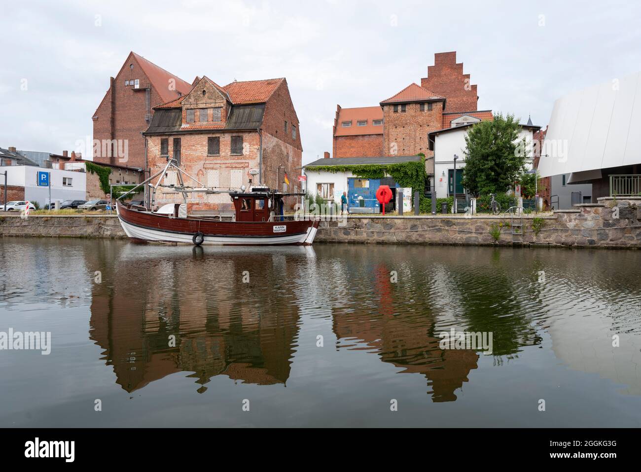 Germania, Meclemburgo-Pomerania occidentale, Stralsund, una barca da pesca è ancorata nel porto della città, dietro di esso si possono vedere vecchi edifici di stoccaggio Foto Stock