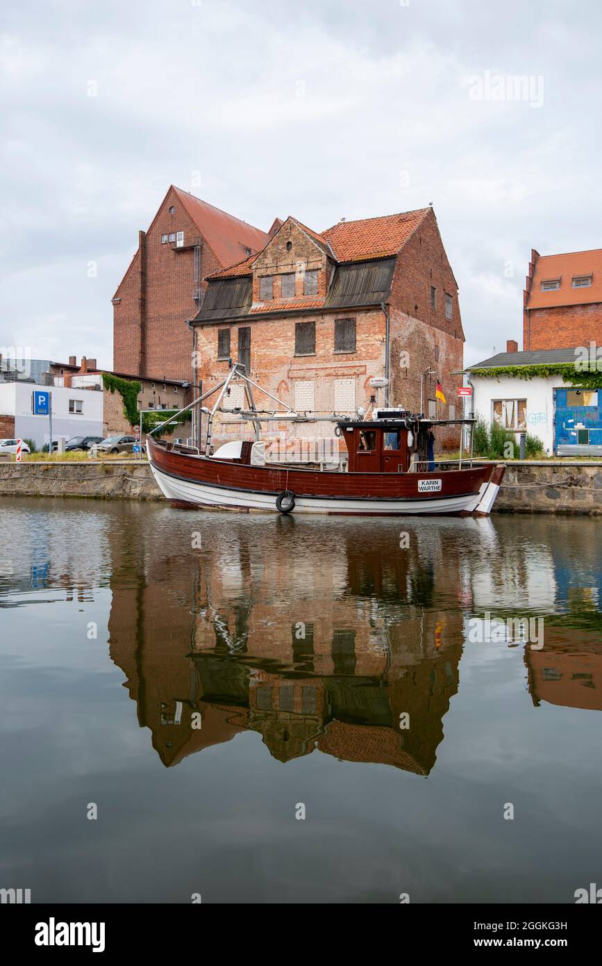 Germania, Meclemburgo-Pomerania occidentale, Stralsund, una barca da pesca è ancorata nel porto della città, dietro di esso si possono vedere vecchi edifici di stoccaggio Foto Stock