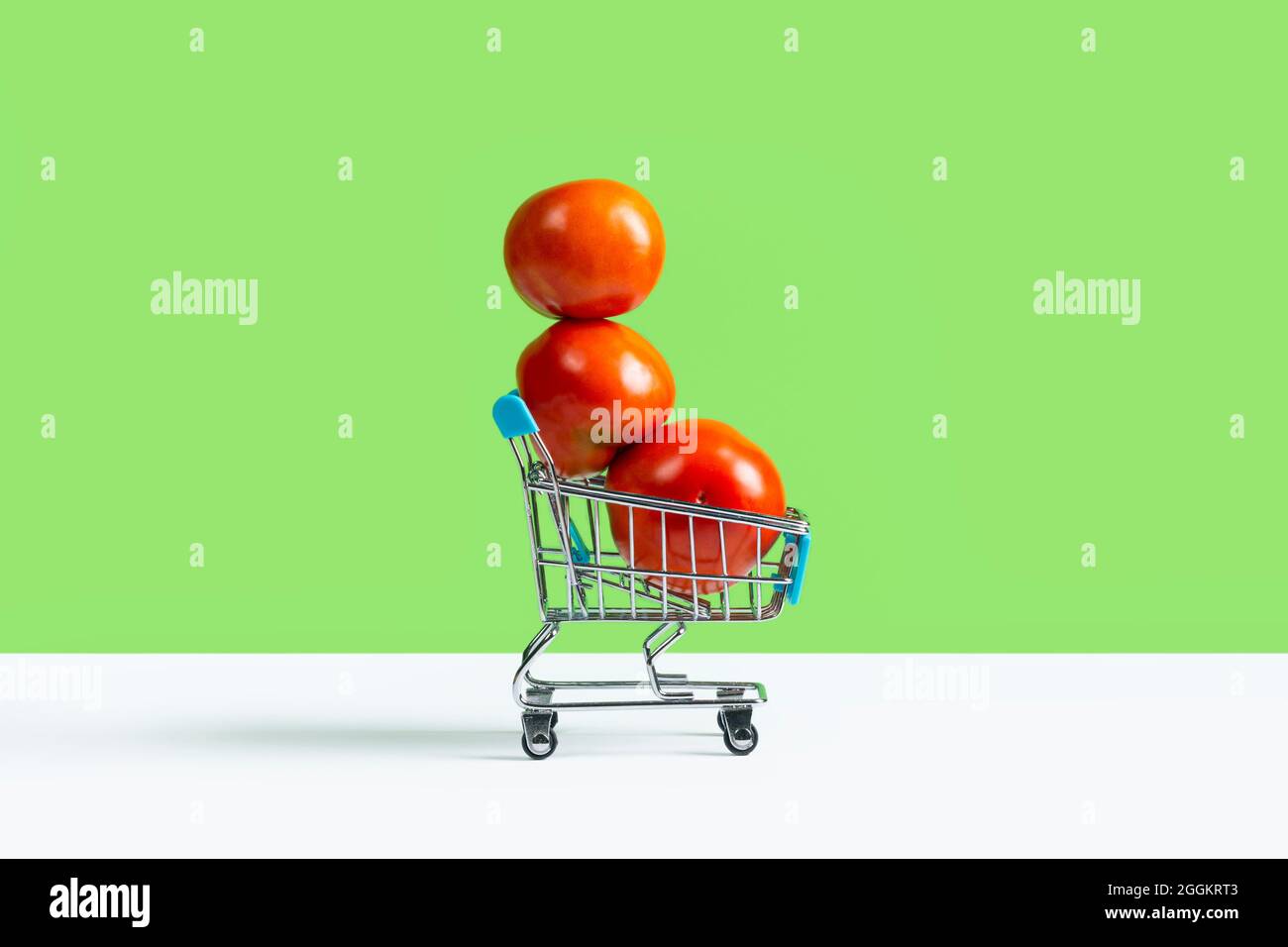 Carrello giocattolo o carrello pieno di grandi pomodori rossi isolato su sfondo verde. Concetto di vendita del raccolto autunnale. Banner con spazio di copia Foto Stock