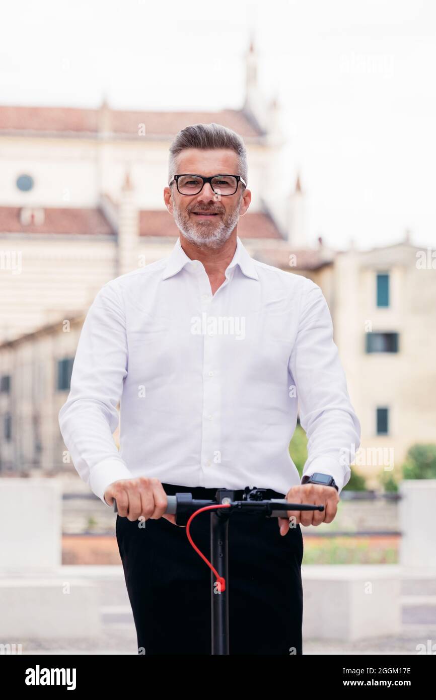 Bel uomo d'affari in tuta a guidare uno scooter elettrico mentre si viaggia per lavoro in città. Concetto di trasporto ecologico Foto Stock