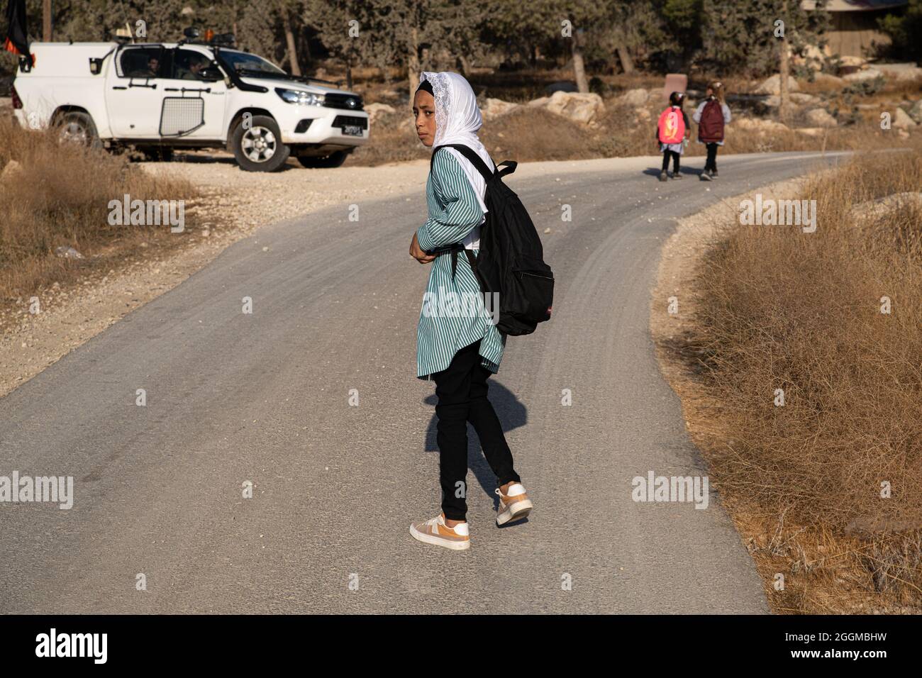 Dal 2004 i bambini del villaggio di Tuba stanno andando a scuola nel vicino villaggio di AT-Tuwani, 2.6 km di distanza - mentre sono stati condotti da un attivista ebraico e un veicolo delle forze di difesa israeliane per proteggerli dagli attacchi violenti da parte dei coloni ebrei religiosi dall'avamposto illegale di Maon Farm, che si trova sul loro cammino verso la scuola. Palestina / Israele, a sud di Hebron. 31 agosto 2021. (Foto di Matan Golan/Alamy Live News) Foto Stock