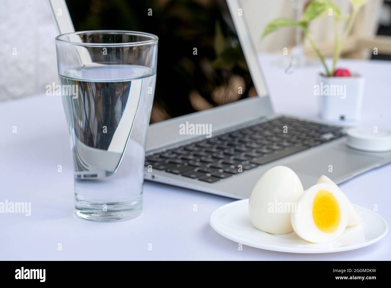 Bicchiere di acqua minerale con uova bollite e computer portatile isolato su sfondo bianco. Dieta casearia alimentazione alimentazione sana. Foto Stock