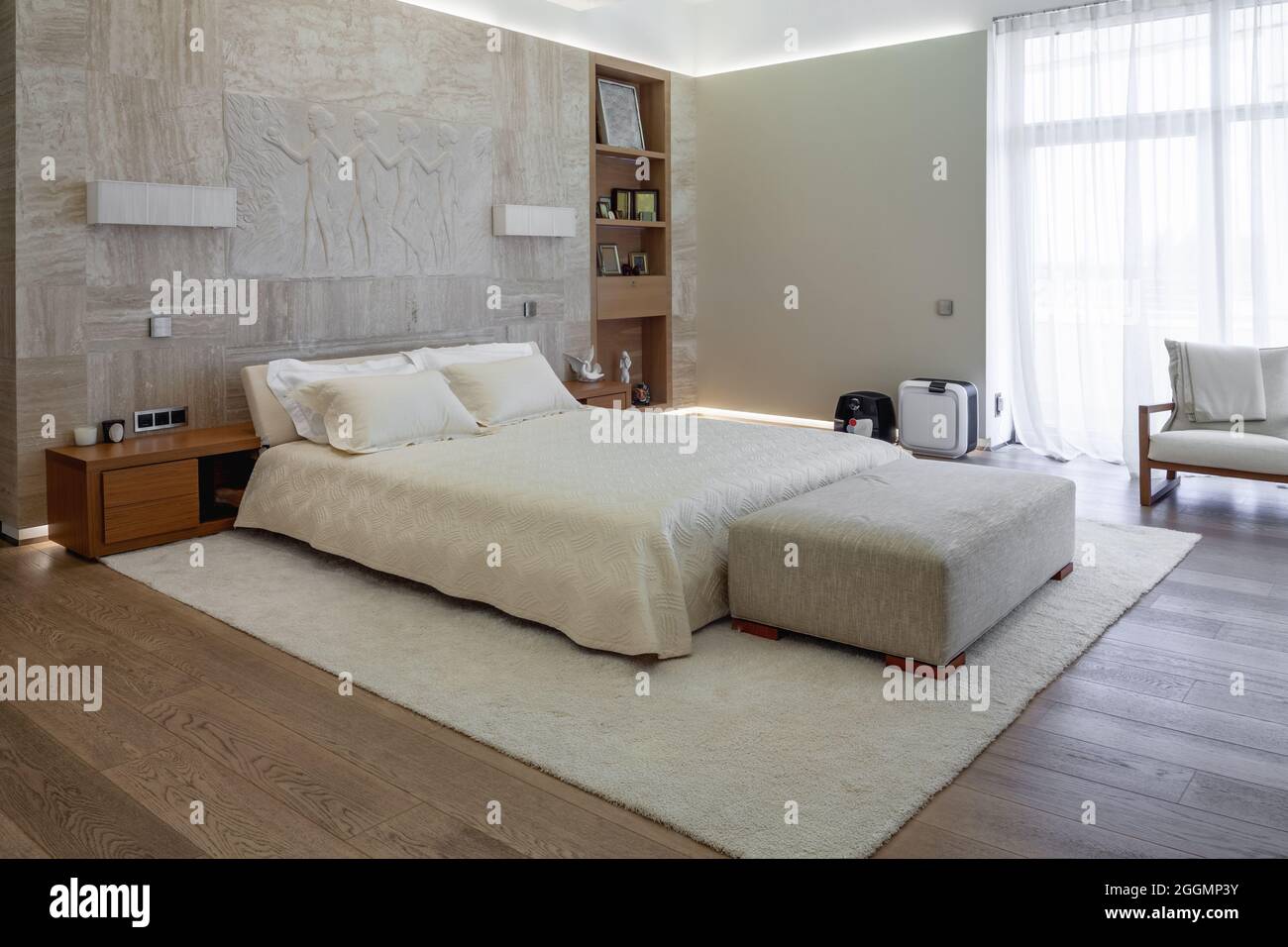 Accogliente camera da letto con ampia finestra e letto matrimoniale vicino alle pareti in marmo decorato con pannelli scultorei Foto Stock