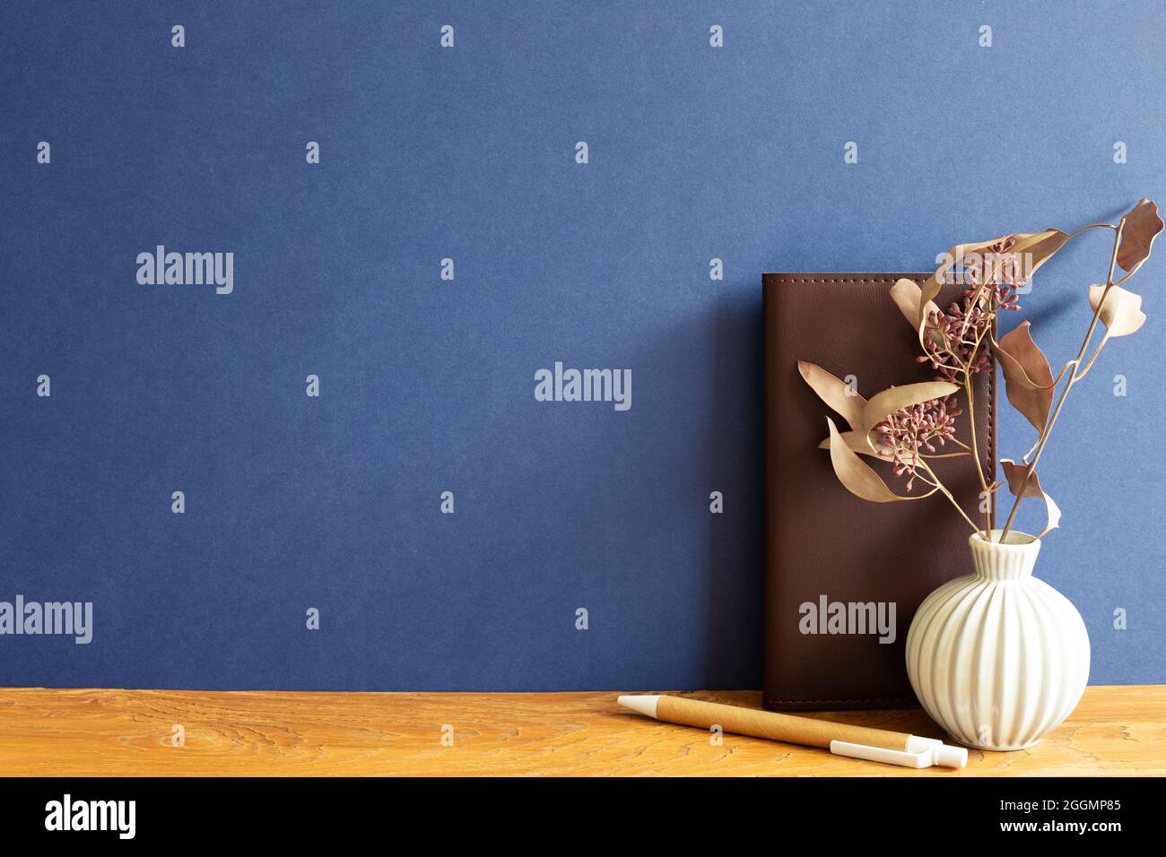Notebook in pelle marrone, penna, fiori secchi su scrivania in legno. Sfondo blu Foto Stock